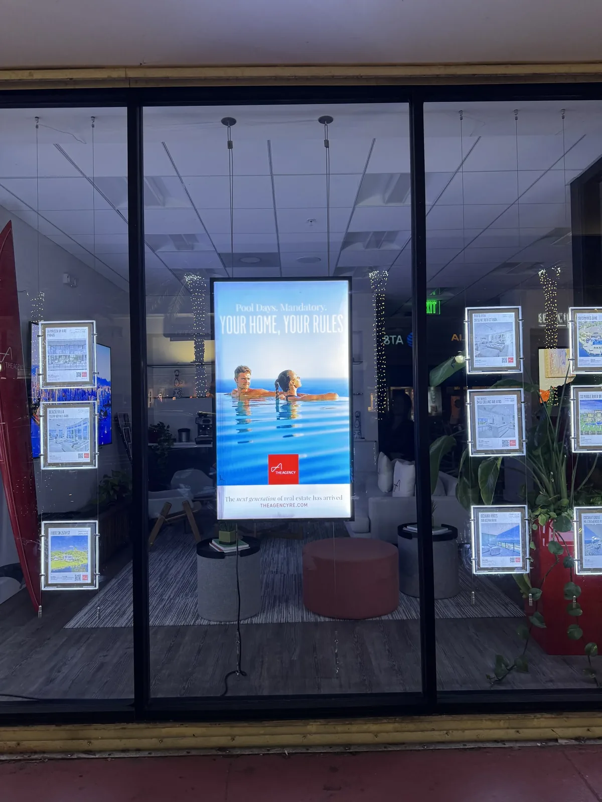 Lobby digital signage: a portrait screen in The Agency real estate office window, visible from the street